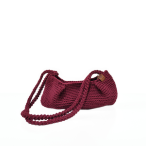 Handmade burgundy dumpling-style crochet bag with double braided straps, set with dried flowers and yarn on a neutral background.