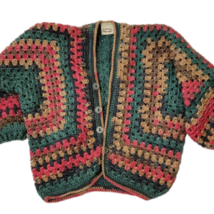 Colorful handmade hexagon baby cardigan crocheted with green, pink, and tan yarn, folded on a white background.