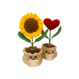 Two handmade crochet potted plants, one with a yellow sunflower and the other with a red heart-shaped flower, both with smiling faces on the pots and inspirational message tags.