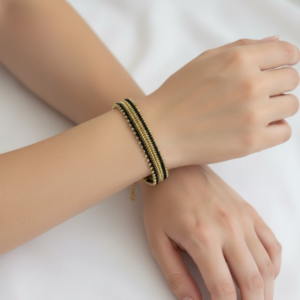 A close-up of a person wearing a handmade black and gold beaded bracelet with a sleek striped pattern.