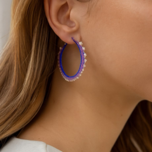 Pair of large, round hoop earrings wrapped with purple and lavender seed beads, creating a serrated or zig-zag pattern. The edges are accented with small silver beads.