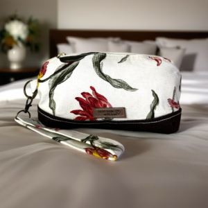 A handmade floral cosmetic pouch on a bed, featuring a "hand made with love" label, with the wrist strap visible, and soft natural light highlighting the product's details.